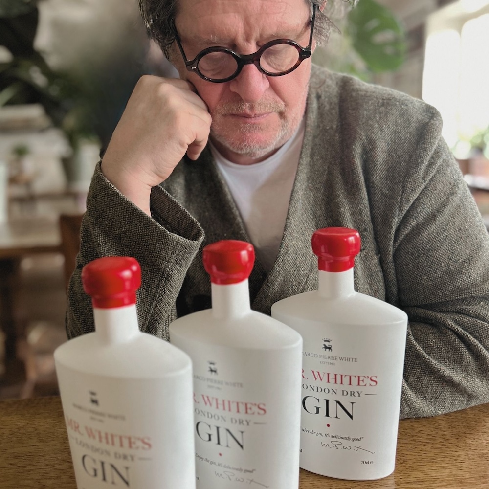 Marco Pierre White looking thoughtful behind bottles of his Mr White's gin